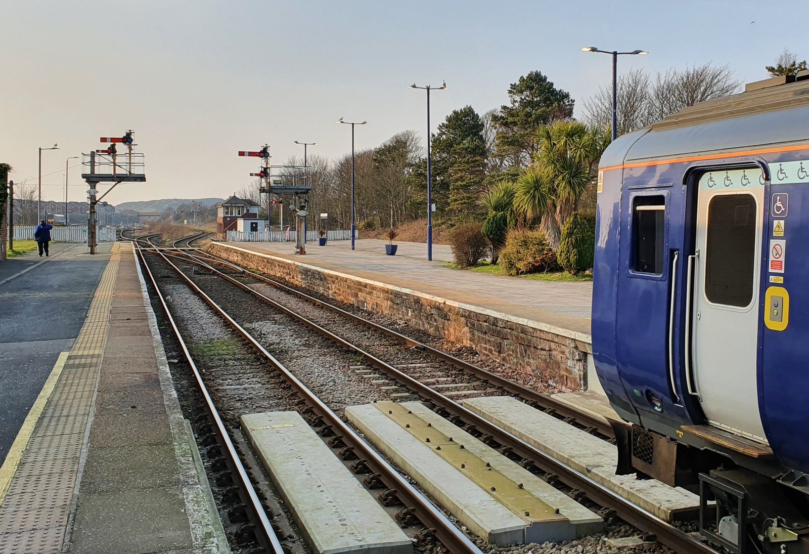 UK railway station platform at sunset with a passenger train preparing to depart